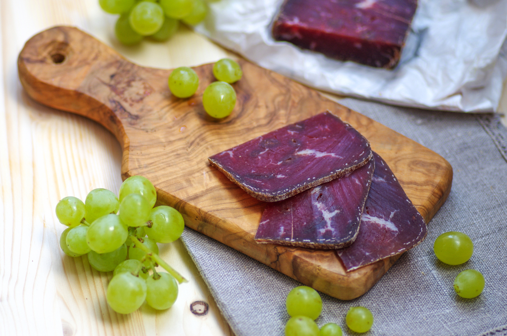 Fines tranches de viande de grisons sur une planche avec raisins